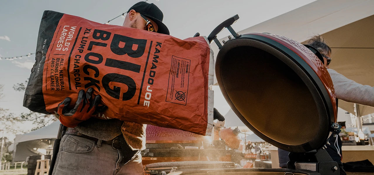 A man standing in front of a tent pours Big Block XL Lump Charcoal from the bag into an open Kamado Joe grill