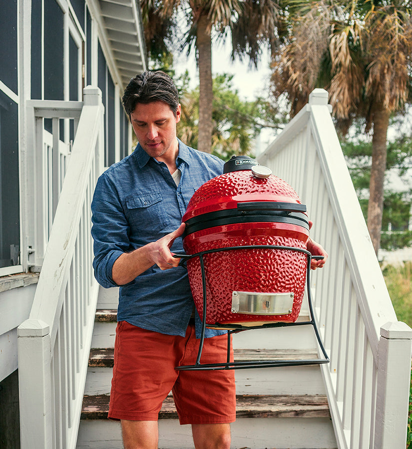 A man wearing a casual blue shirt and orange shorts carries a Joe Jr down wooden stairs leading from a screened patio to the ground.