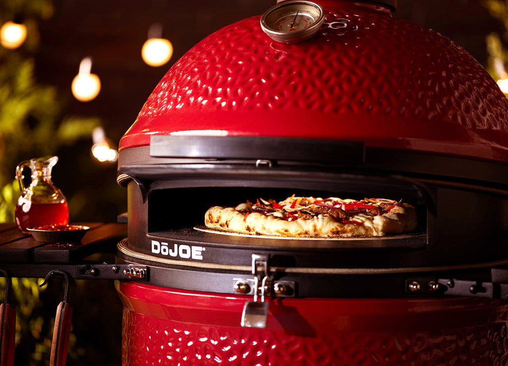 A pizza cooks in a DoJoe installed in a Kamado Joe grill