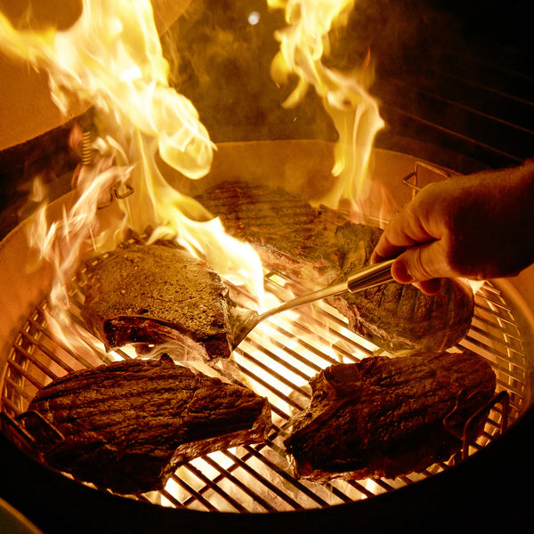 Flames flare up around seared steaks cooking in a Kamado Joe grill