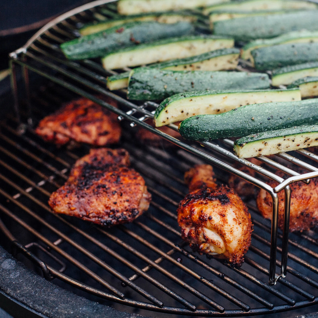 Slices of spice zucchini cook on the grill expander above an assortment of chicken pieces.