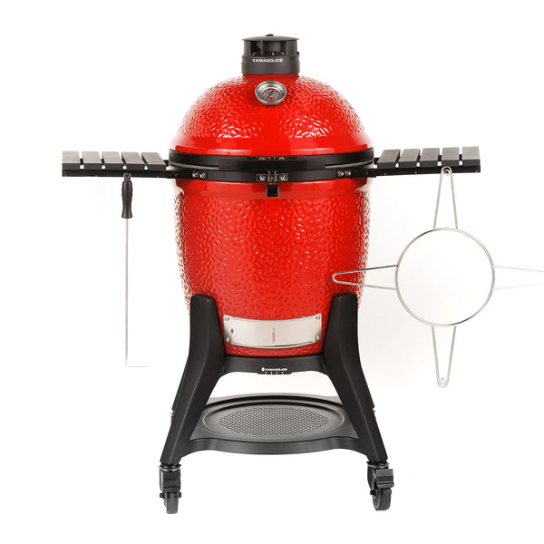 A red Classic Joe III grill with black side shelves, Kontrol Tower top vent, and heavy-duty cart with wheels. A temperature gauge is built into the grill dome. A sliding steel access door is built into the bottom of the grill base. Ash scraper and accessory rack hang from the side shelves