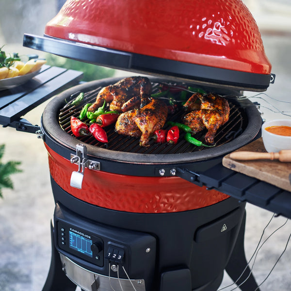 Chicken quarters and whole chili peppers  grilling on a partially open Konnected Joe grill.