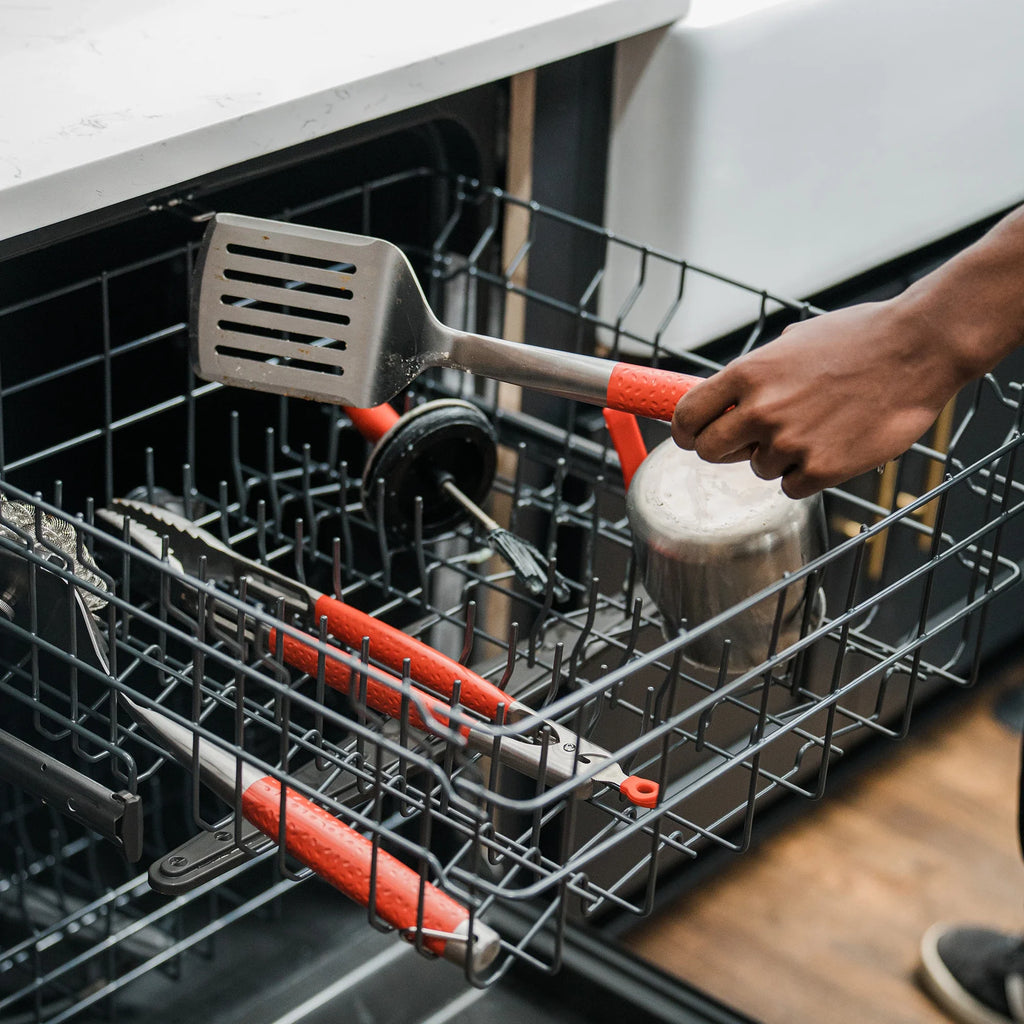 Loading the tools into a the top rack of a dishwasher. The tongs, spatula, brush, basting pot and basting brush all fit together in the top rack.