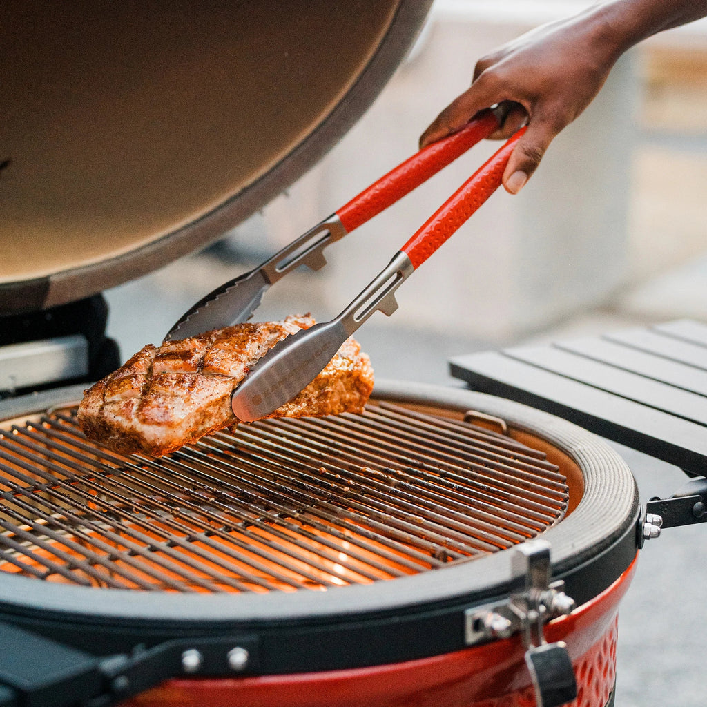 Someone using the tongs to remove a salmon filet from the cooking grate