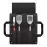Set of three Kamado Joe kitchen tools (tongs, spatula, bristle brush) in a black carrying case with red stitching and side handled on a white background