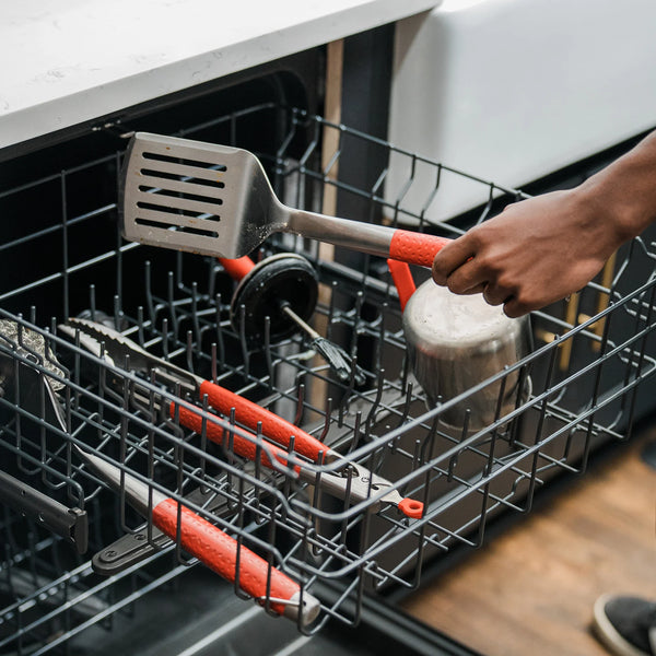Loading the tools into a the top rack of a dishwasher. The tongs, spatula, brush, basting pot and basting brush all fit together in the top rack.