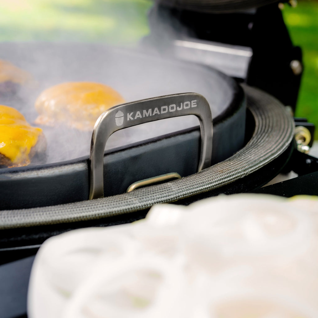 Edge view of griddle while cooking cheeseburgers showing the loop handle extending above the grill