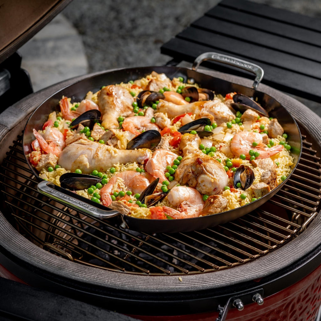 Paella with shrimp, mussels, chicken legs and peas cooks in a Karbon Steel paella pan while sitting on the wire grill of a Kamado Joe grill