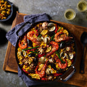 The Karbon Steel paella pan sits on a towel and wooden board for serving
