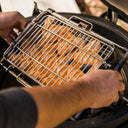 A man uses 2 hands to mount a JoeTisserie basket full of wings into the JoeTisserie ring