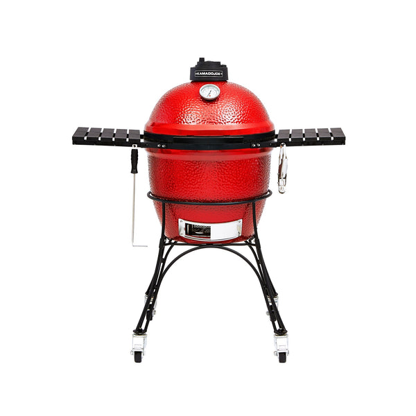 Red Classic Joe I Kamado grill with 2 black side shelves, black top vent, a temperature gauge built into the grill dome, and a sliding chrome door in the base. The grill sits in a black cart with wheels.