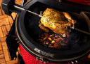 A whole chicken roasts on a JoeTisserie. A pan of chopped vegetables sits below the chicken to catch the drippings.